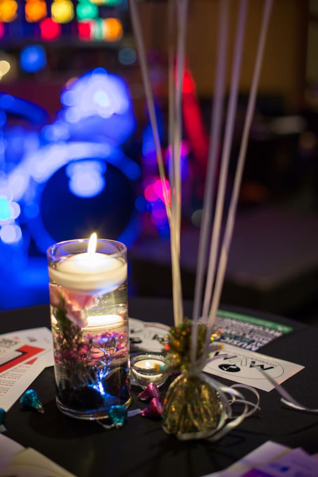 Candle centerpiece with floral accents and colorful decor at the Love Bomb 2017 event supporting My Voice Music, illuminated by ambient lighting in the background.